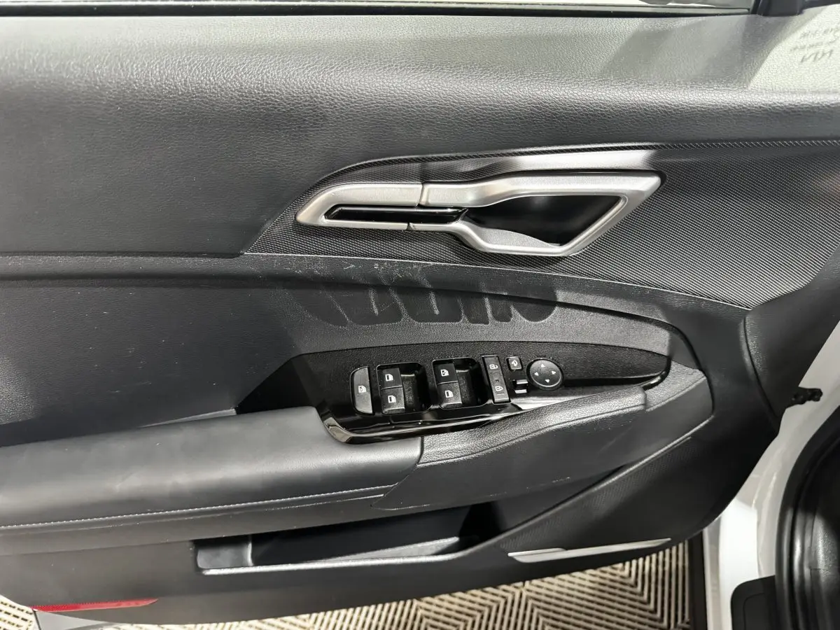 Vue rapprochée de la porte avant gauche blanche du Kia Sportage 2024, avec commandes électriques et poignée argentée.