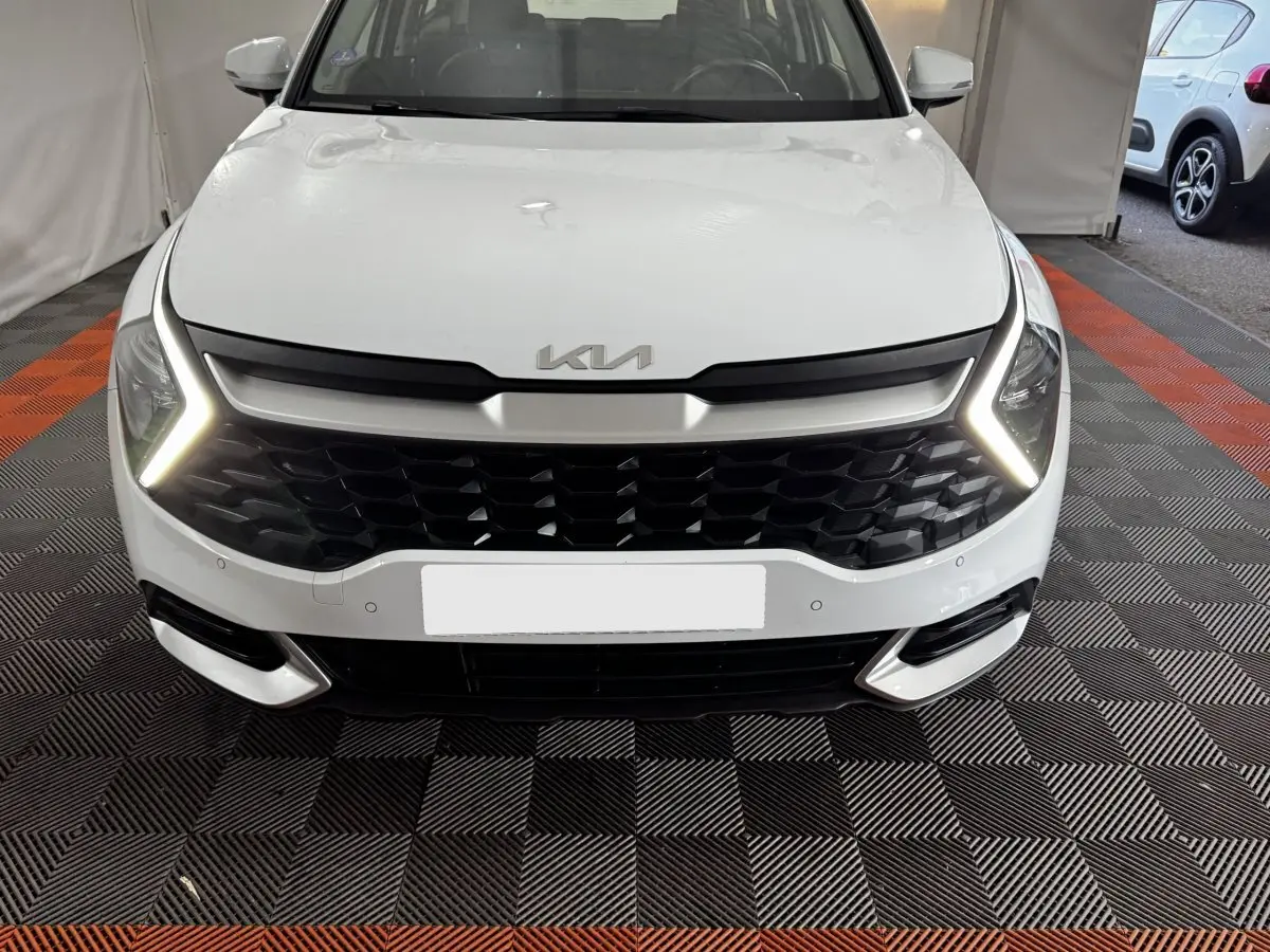 Vue frontale d'un KIA Sportage blanc 2024 avec calandre noire et feux diurnes LED en forme de flèche.