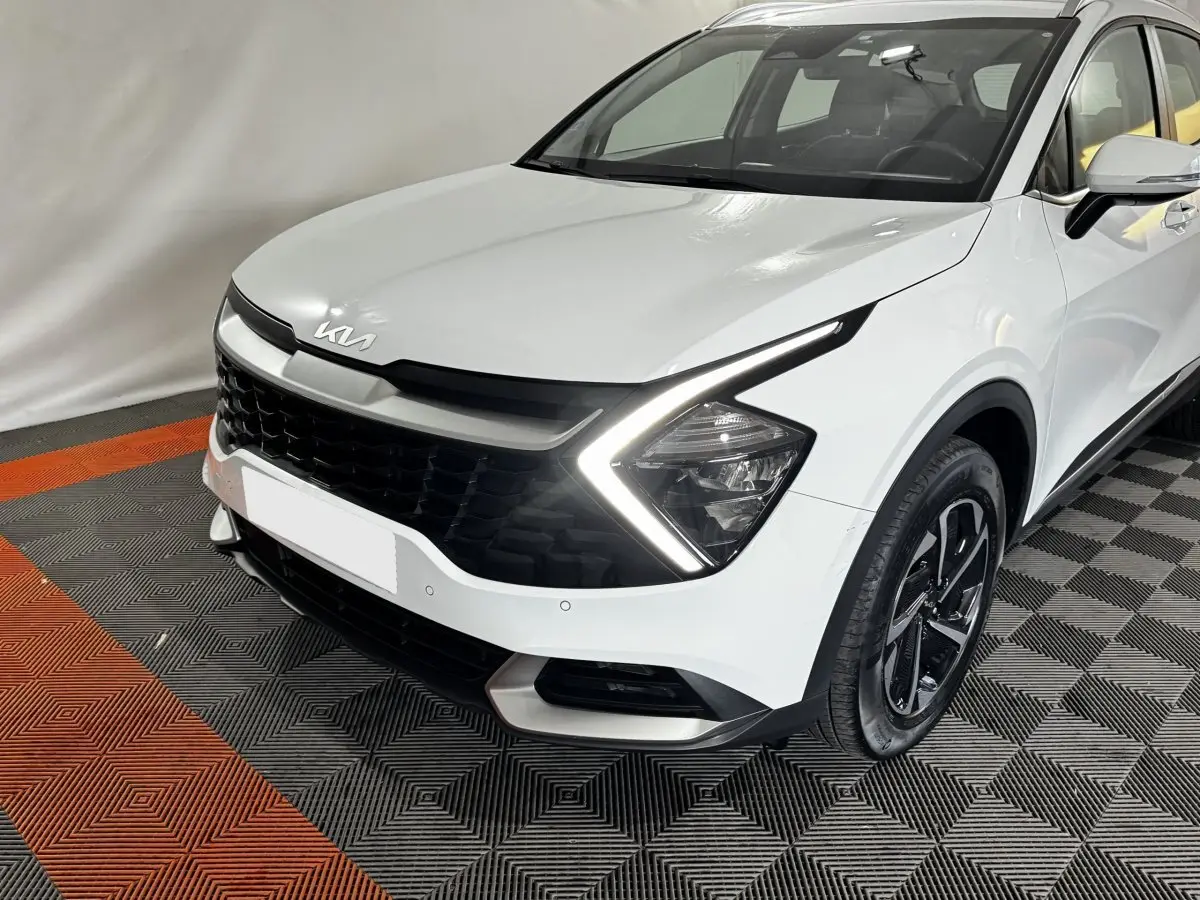 KIA Sportage blanc vu de 3/4 avant droit avec feux LED en forme de flèche et calandre noire distinctive.