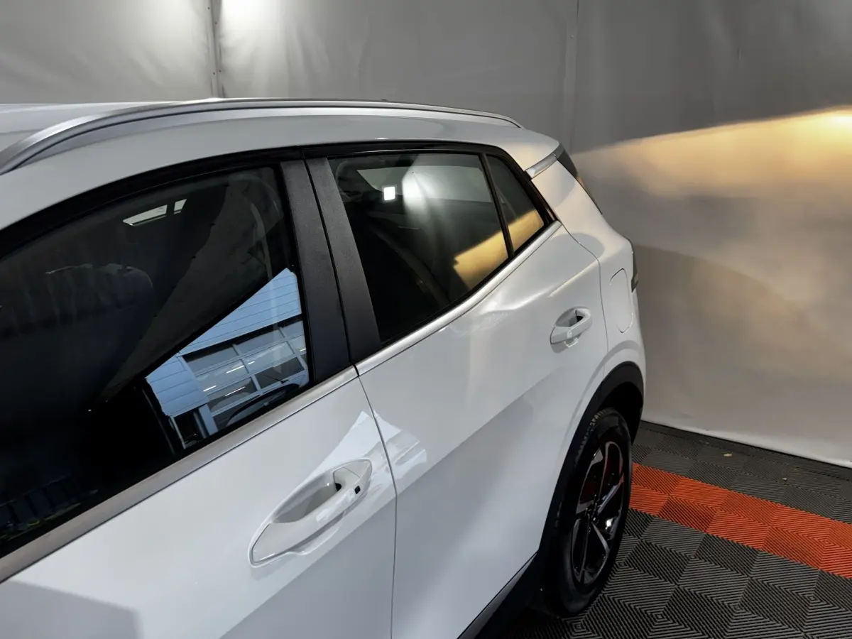 Vue côté droit arrière du Kia Sportage blanc 2024, avec poignées de porte et jante noire visible sur sol à motifs rouges et gris.