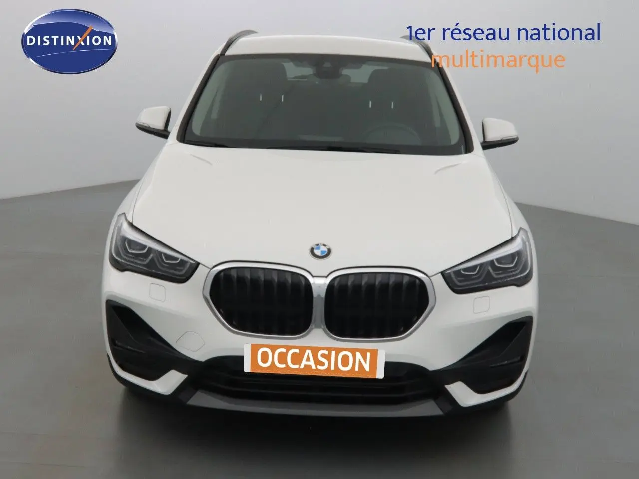 Vue frontale d'un BMW X1 blanc Alpine Metal avec calandre noire et phares LED marqués dans un studio.