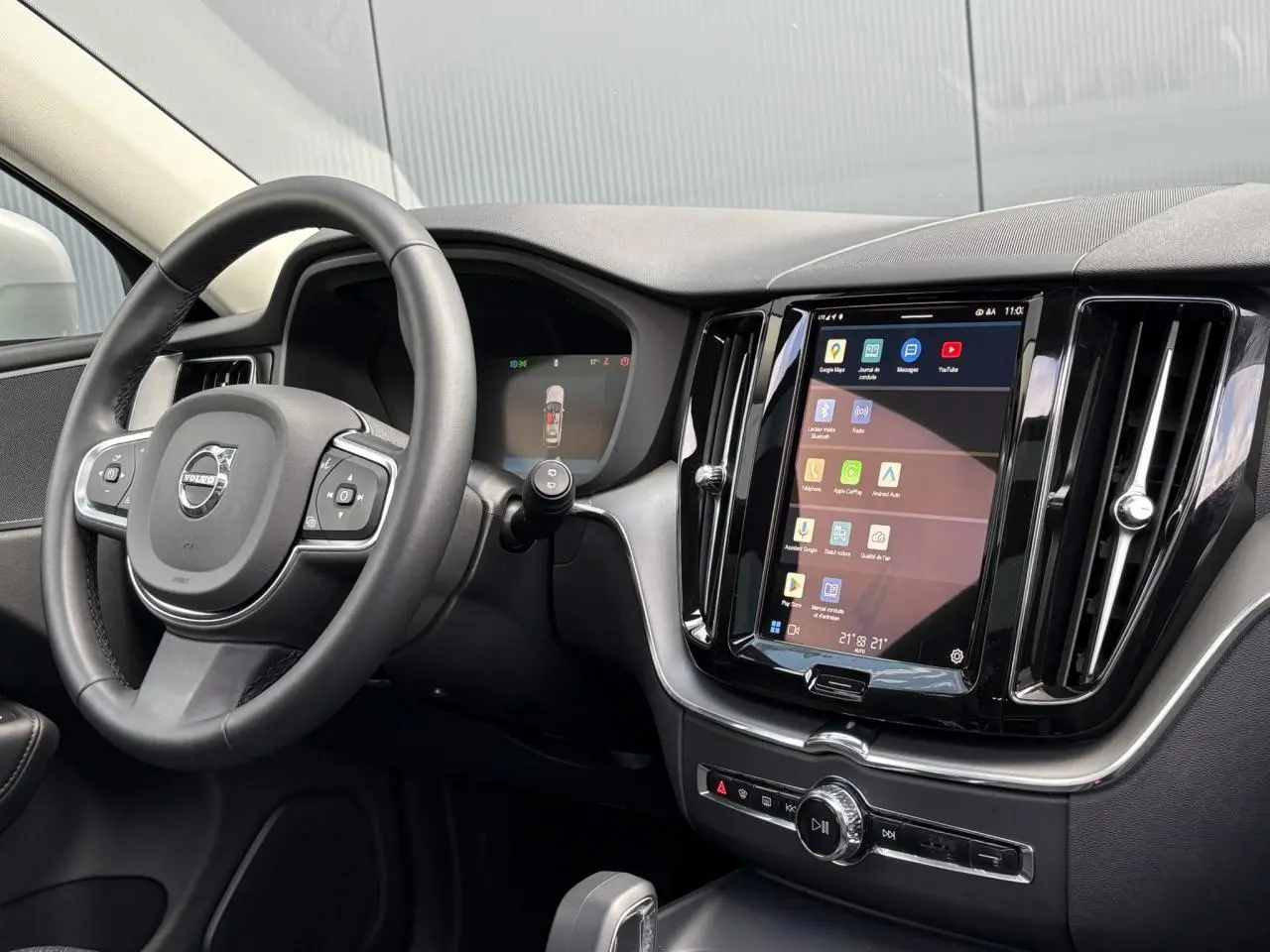 Vue intérieure côté conducteur du Volvo XC60 gris silver 2024, avec volant simili-cuir et écran tactile vertical.