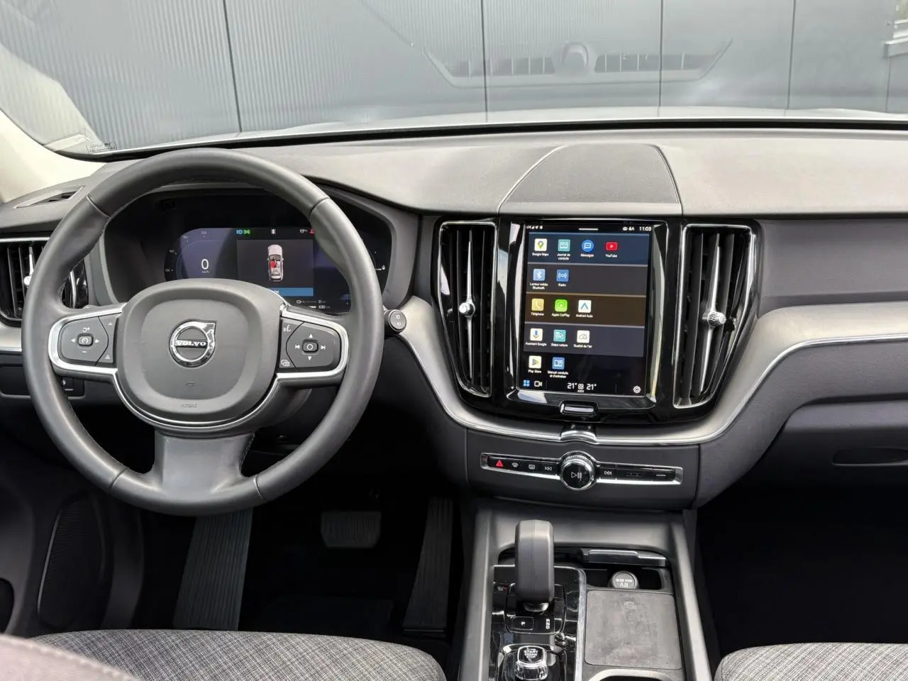 Vue intérieure du tableau de bord du Volvo XC60 gris Silver 2024, avec volant 3 branches et écran tactile vertical.