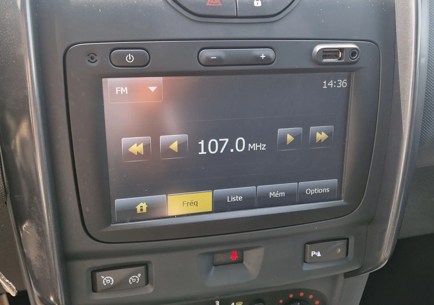 Gros plan sur l'écran tactile central du tableau de bord du Dacia Duster gris foncé, affichant la radio FM à 107.0 MHz.