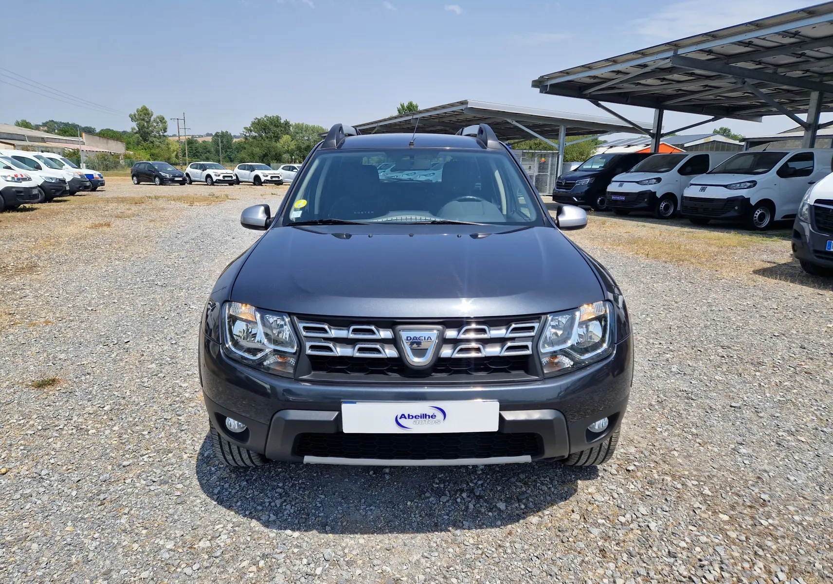 Vue de face d'un Dacia Duster 1.5 DCI 110 Prestige gris foncé métal, avec calandre chromée et phares allumés.