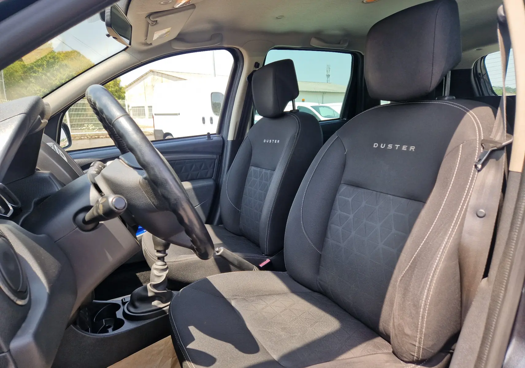 Vue intérieure côté conducteur du Dacia Duster 2015, sièges noirs avec logo DUSTER et volant en cuir.