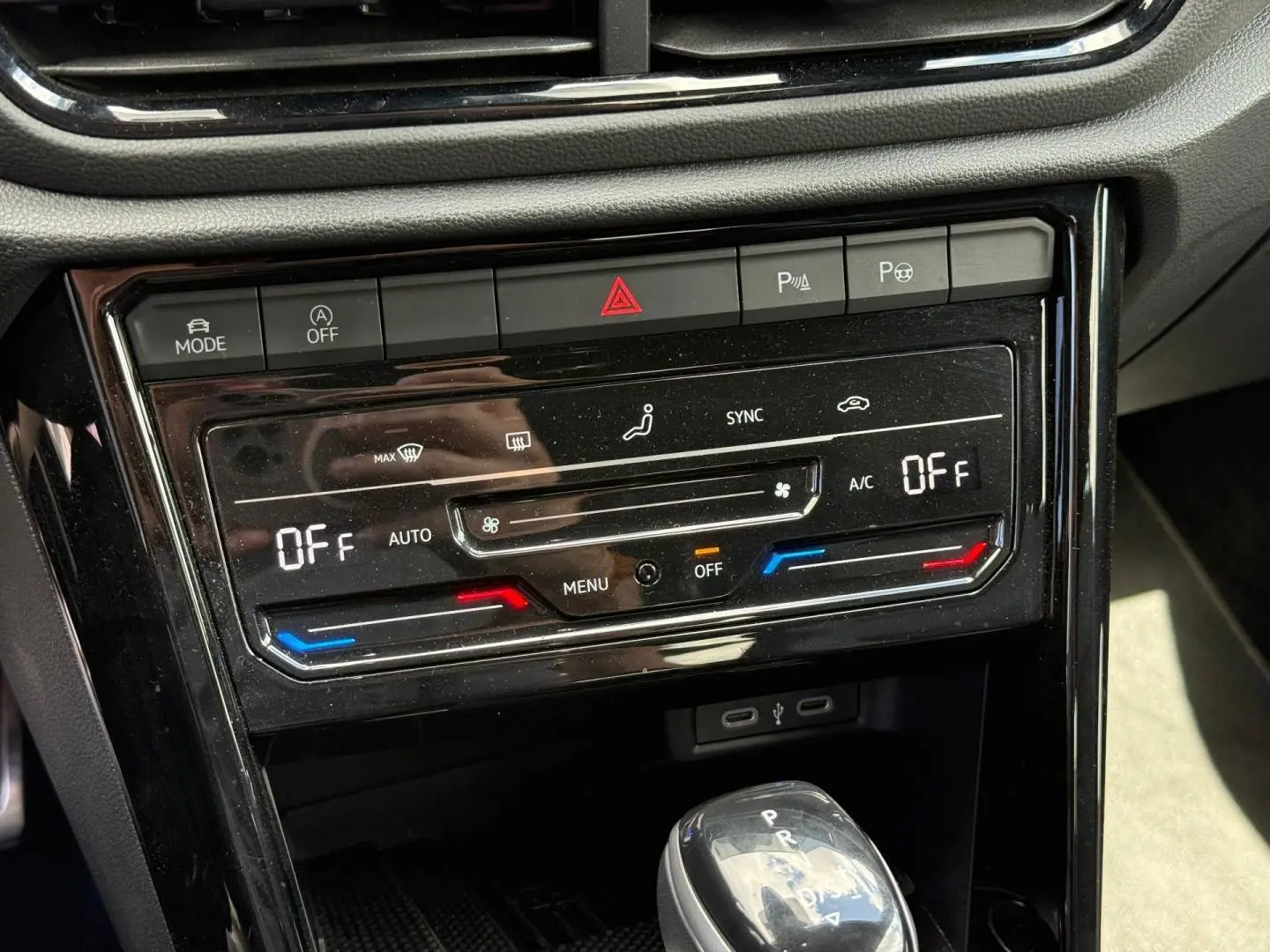 Vue rapprochée du tableau de bord noir brillant du Volkswagen T-Roc 2025, montrant la climatisation digitale et le levier de vitesse automatique.