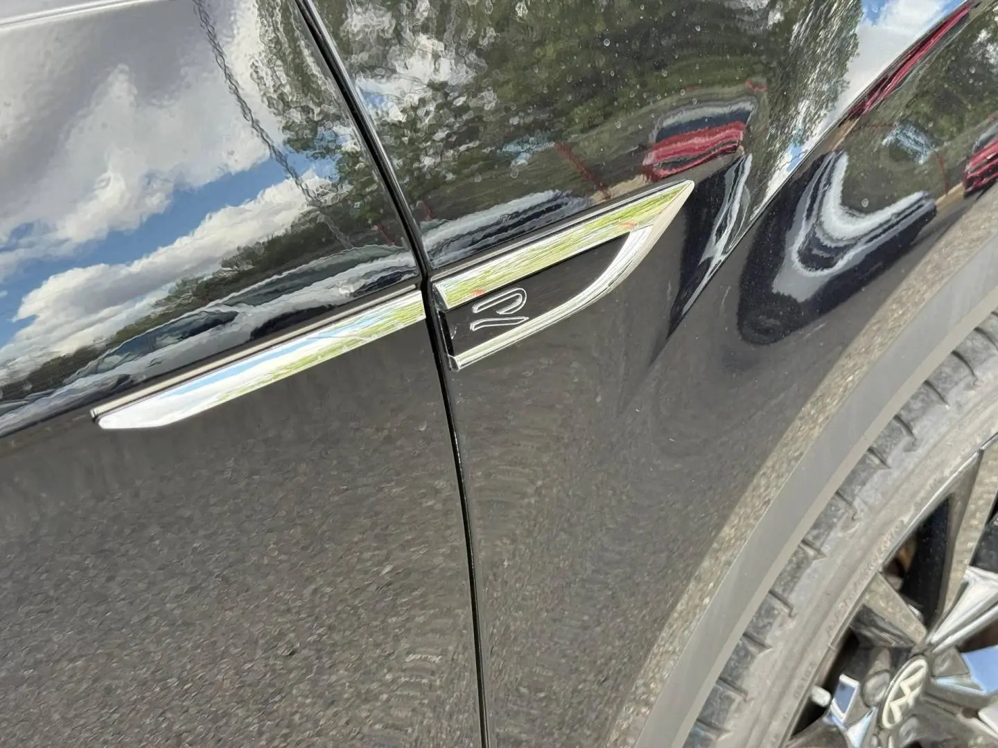 Gros plan sur l’aile avant droite noire nacrée du Volkswagen T-Roc avec logo R et jante alu visible.