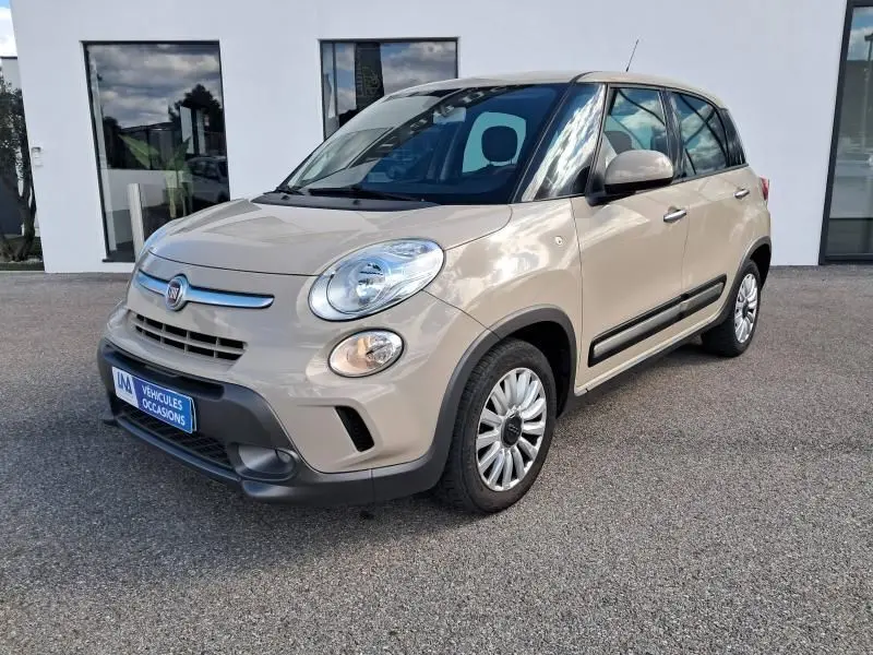 Fiat 500L beige vue 3/4 avant droit, avec phares ronds et protections noires sur les bas de caisse.