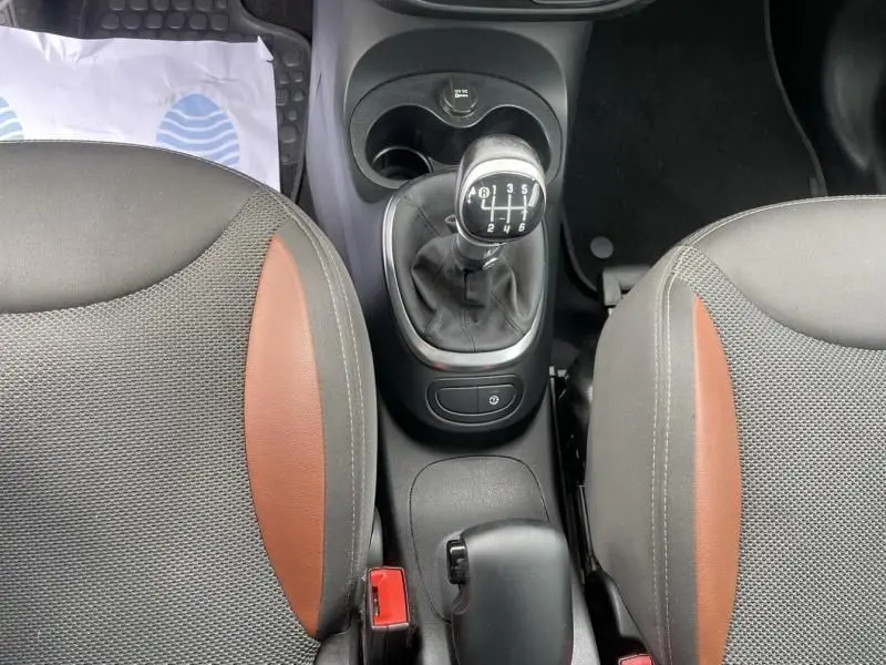 Vue plongeante sur la console centrale d'une Fiat 500L beige, mettant en valeur la boîte manuelle et les sièges bicolores gris et marron.