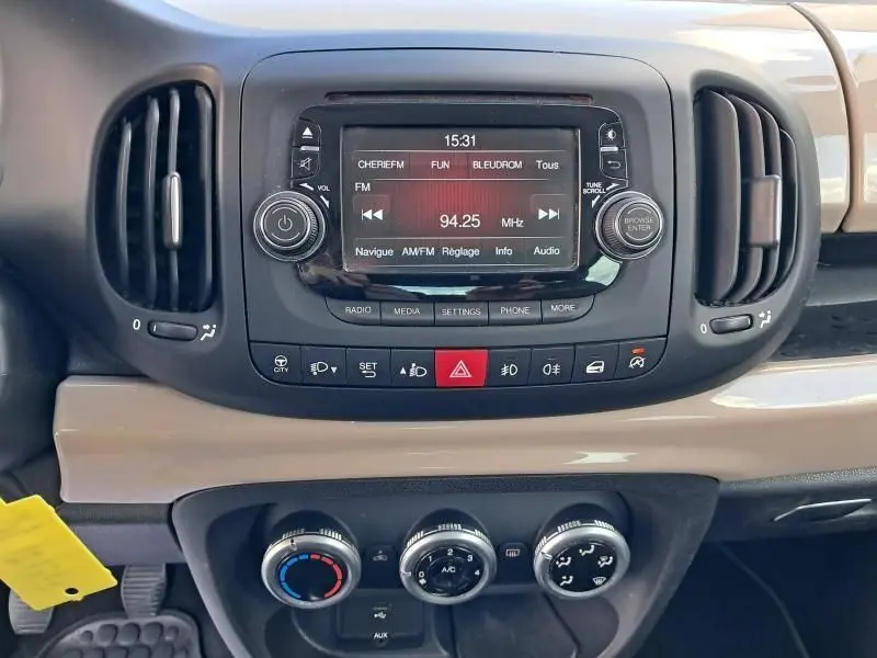 Tableau de bord beige d'une Fiat 500L 1.6 Multijet 2014 avec écran radio et commandes climatiques visibles en gros plan.