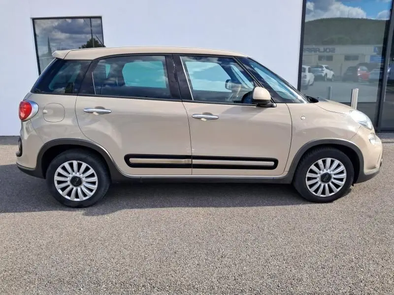Profil côté gauche d'une FIAT 500L beige 2014 avec baguettes noires et jantes multibranches sur parking.