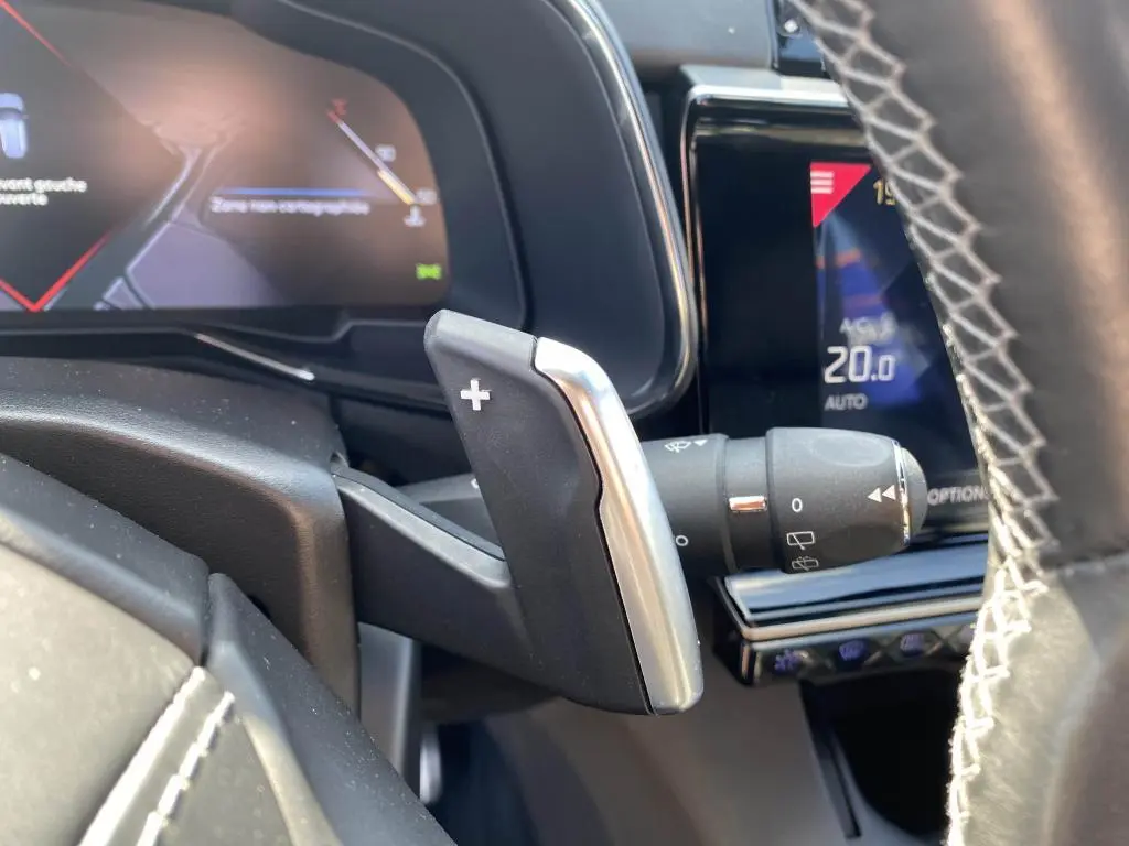 Gros plan sur la palette de changement de vitesse + du DS7 Crossback jaune clair, avec tableau de bord numérique en arrière-plan.