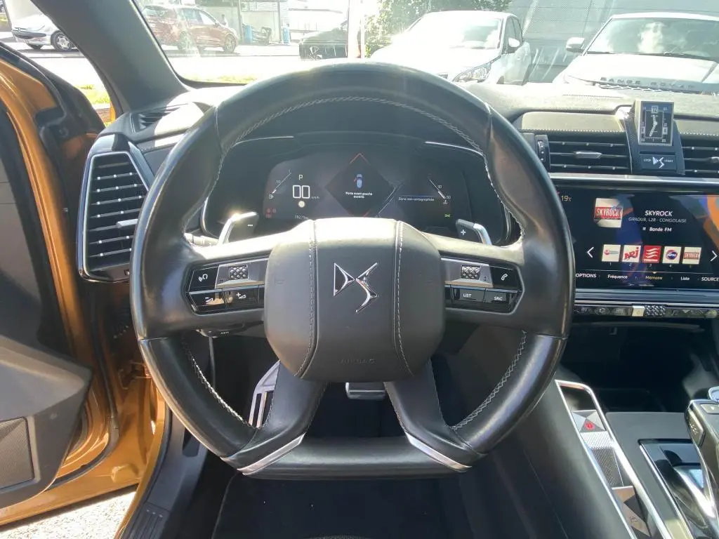 Vue centrée sur le volant cuir DS d'un DS7 Crossback jaune clair, avec tableau de bord numérique et écran tactile visible.