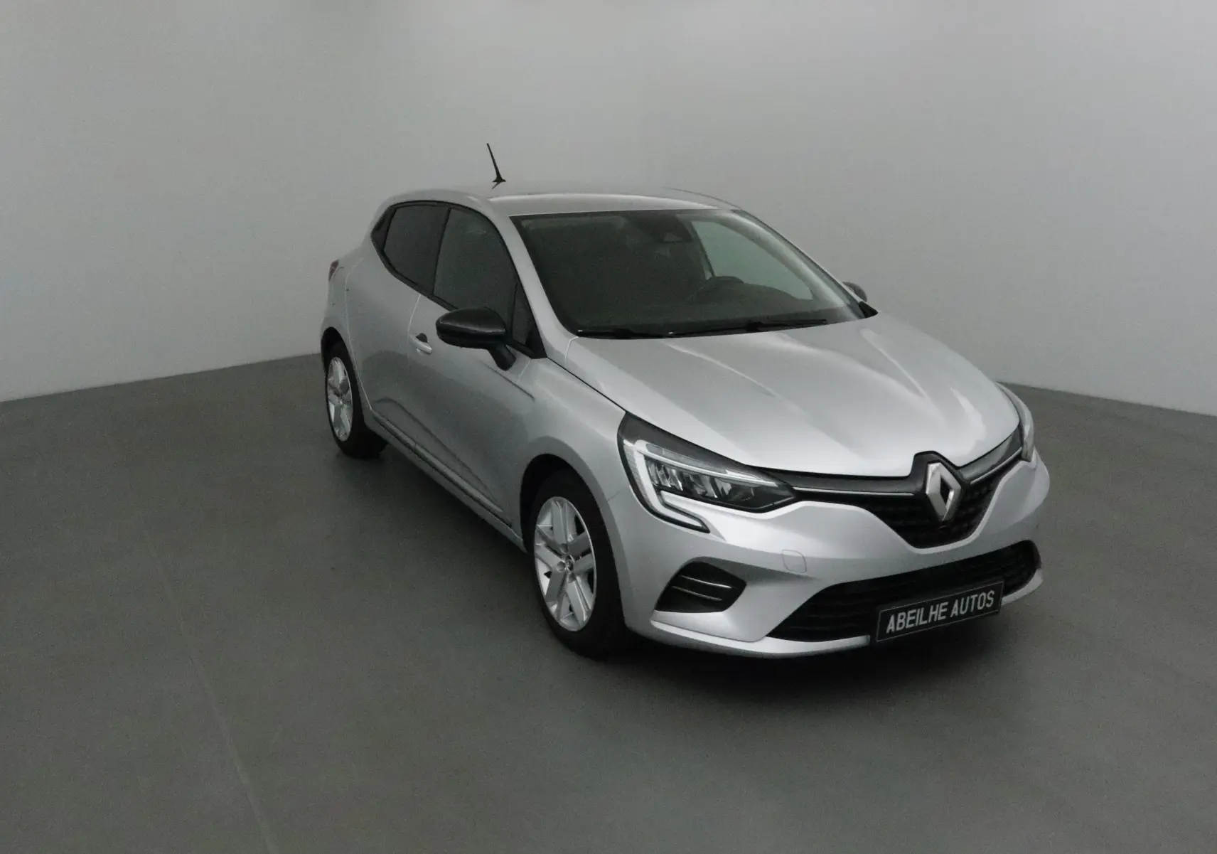 Renault Clio V gris platine vue 3/4 avant droit, avec phares LED et calandre noire distinctive.