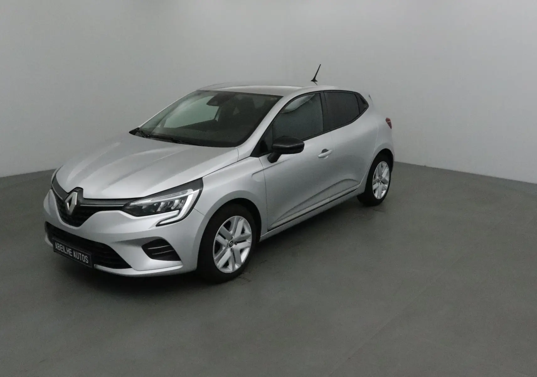Renault Clio V gris platine vue 3/4 avant droit dans un studio, avec phares LED et jantes alliage.