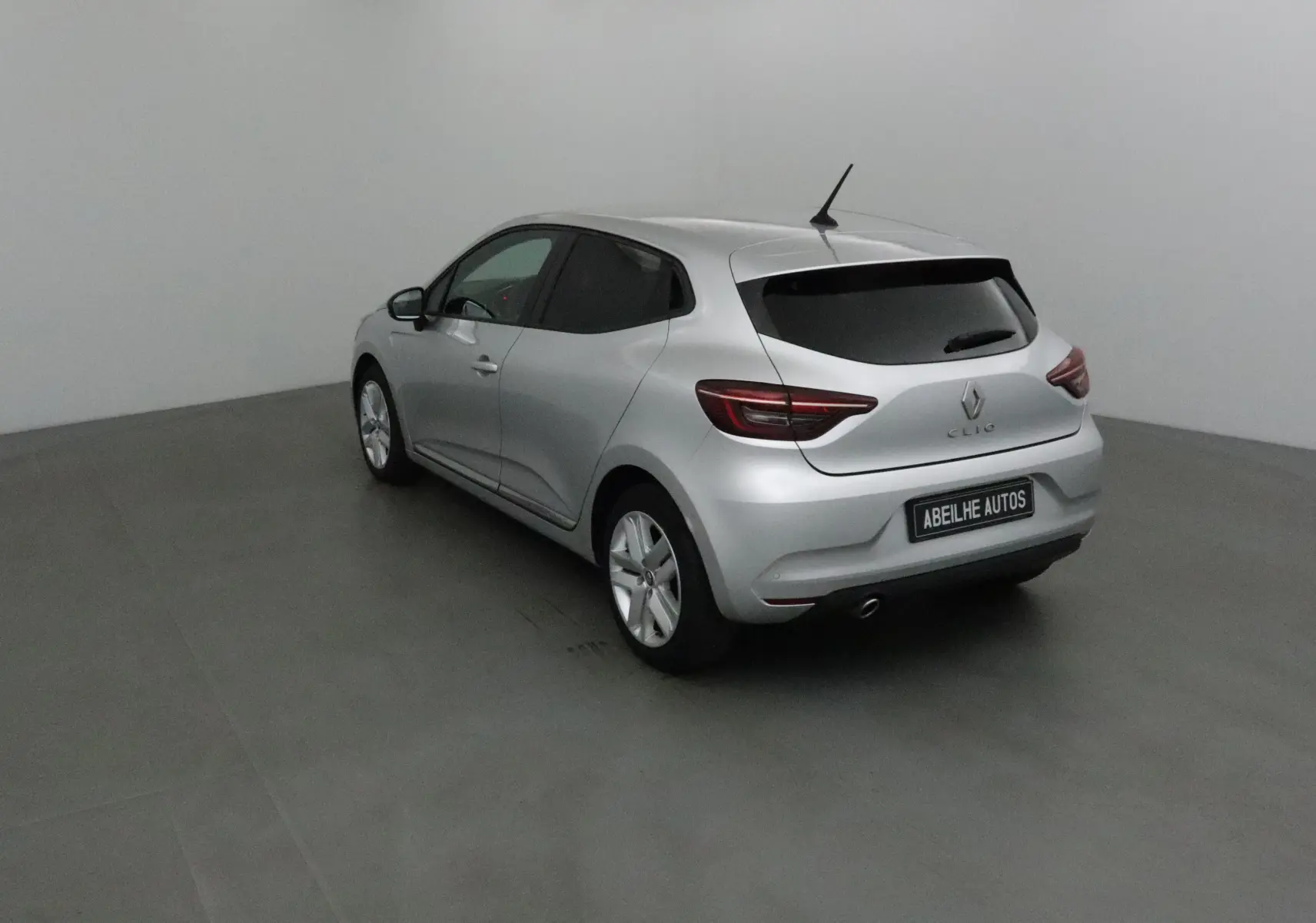 Renault Clio V gris platine vue 3/4 arrière droit dans un studio, avec vitres teintées et jantes alliage.