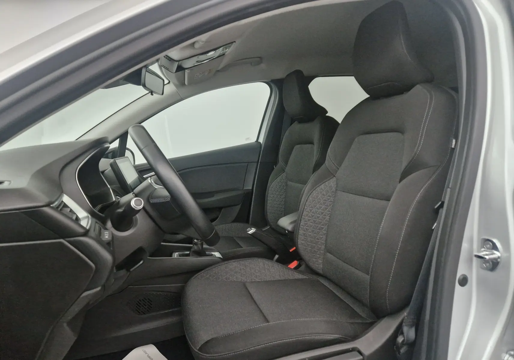 Intérieur de la Renault Clio V gris platine, vue côté gauche sur les sièges avant en tissu noir avec motifs géométriques.