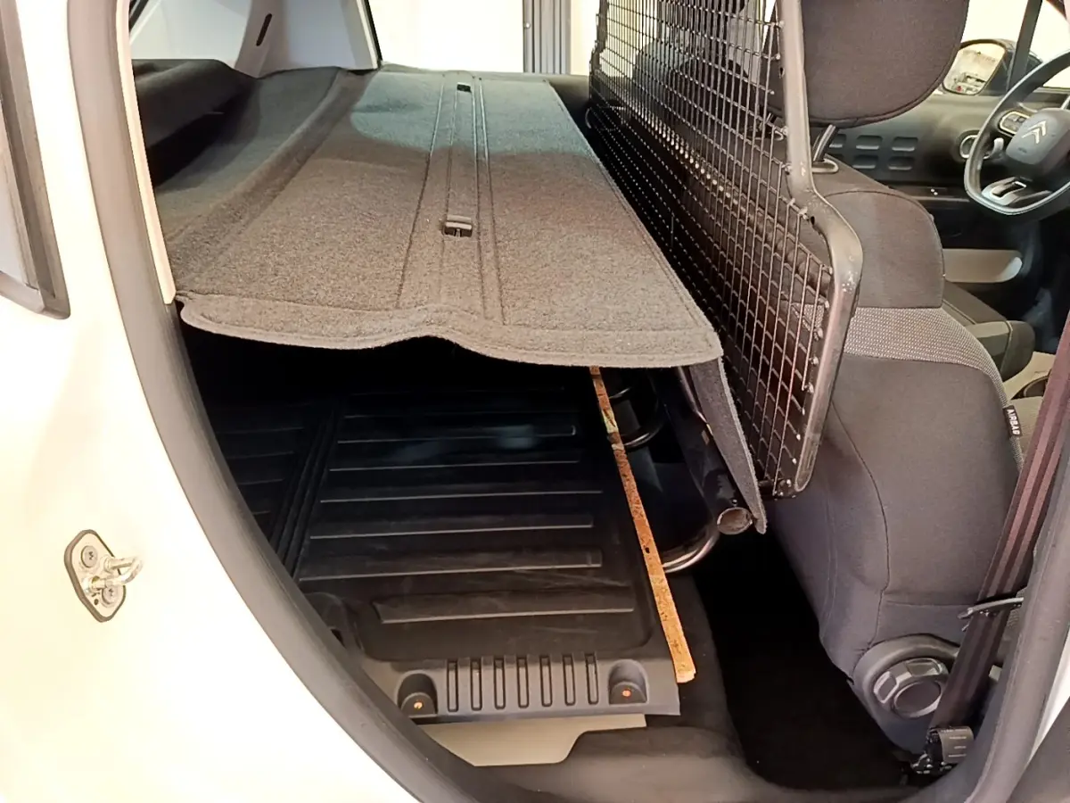 Vue intérieure arrière droite d'une Citroën C3 blanche avec séparation grillagée et plancher de coffre visible.