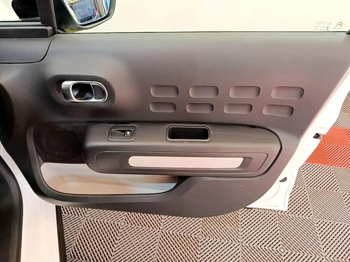 Vue rapprochée de la porte avant gauche blanche d’une Citroën C3 2022 avec poignée intérieure chromée et panneau noir texturé.