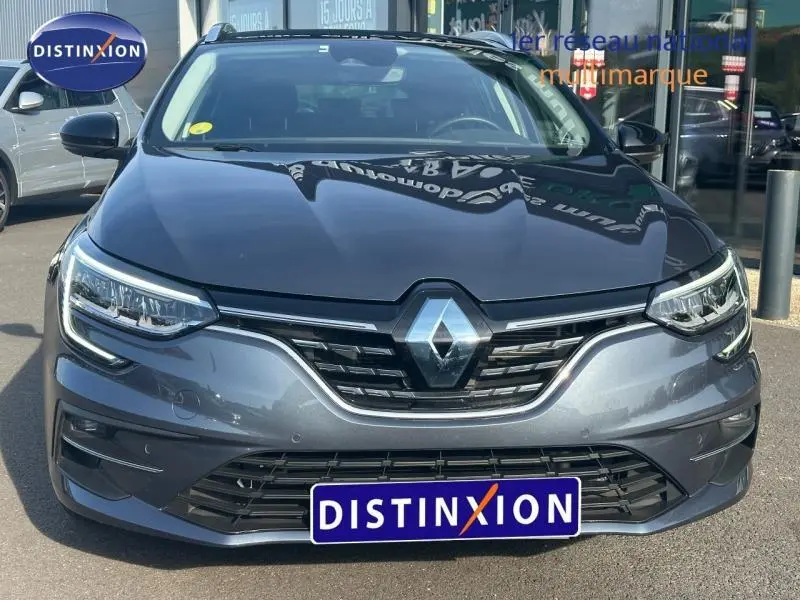 Vue avant rapprochée d’une Renault Mégane Break 2024 gris titanium avec calandre chromée et phares LED allumés.