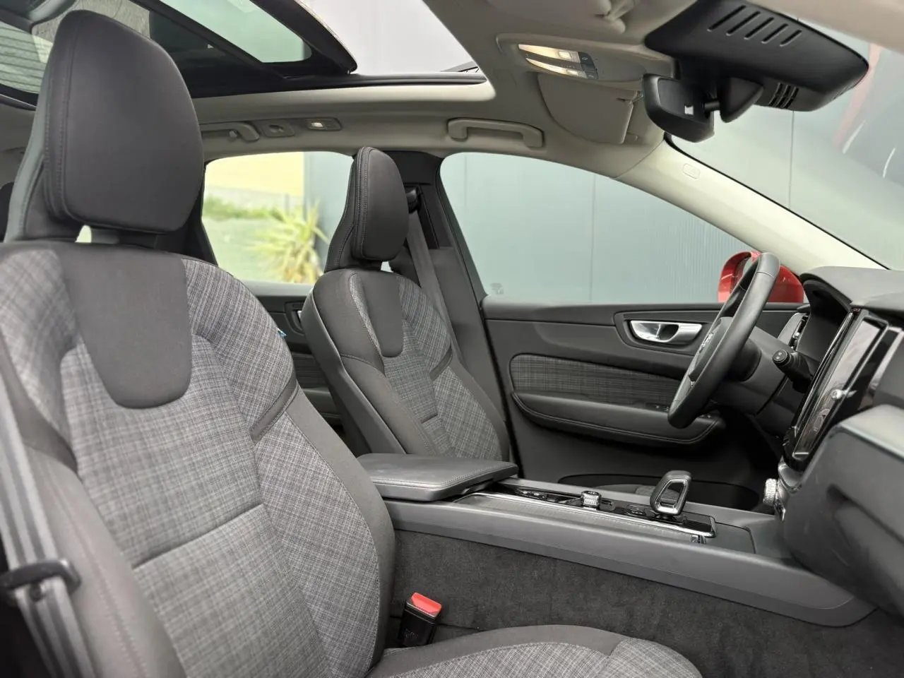Vue intérieure côté conducteur du Volvo XC60 2024, sièges tissu gris à motif, toit ouvrant panoramique et volant simili-cuir.