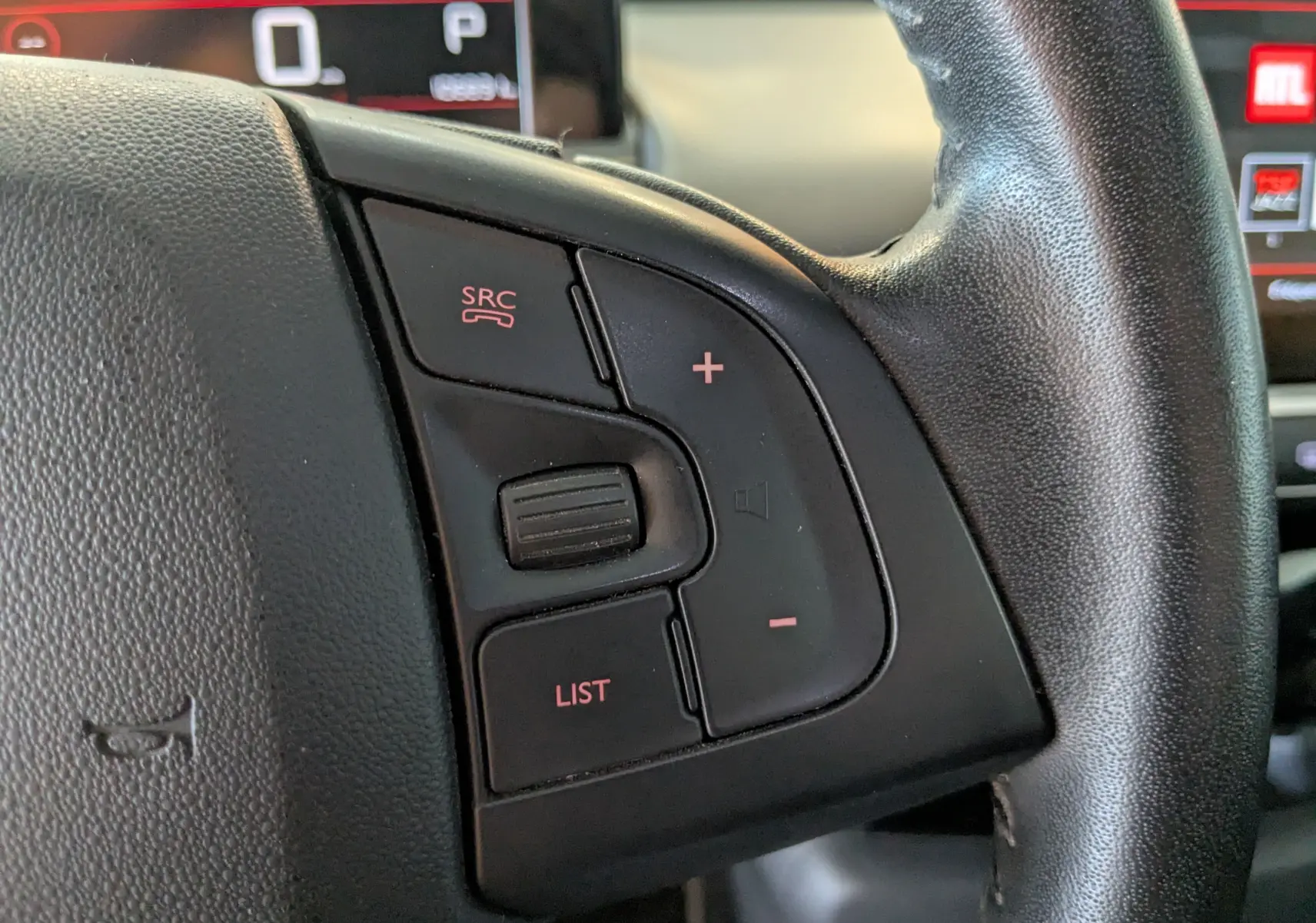 Gros plan sur les commandes audio au volant noir d'une Citroën C4 Cactus blanche, tableau de bord et écran en arrière-plan.