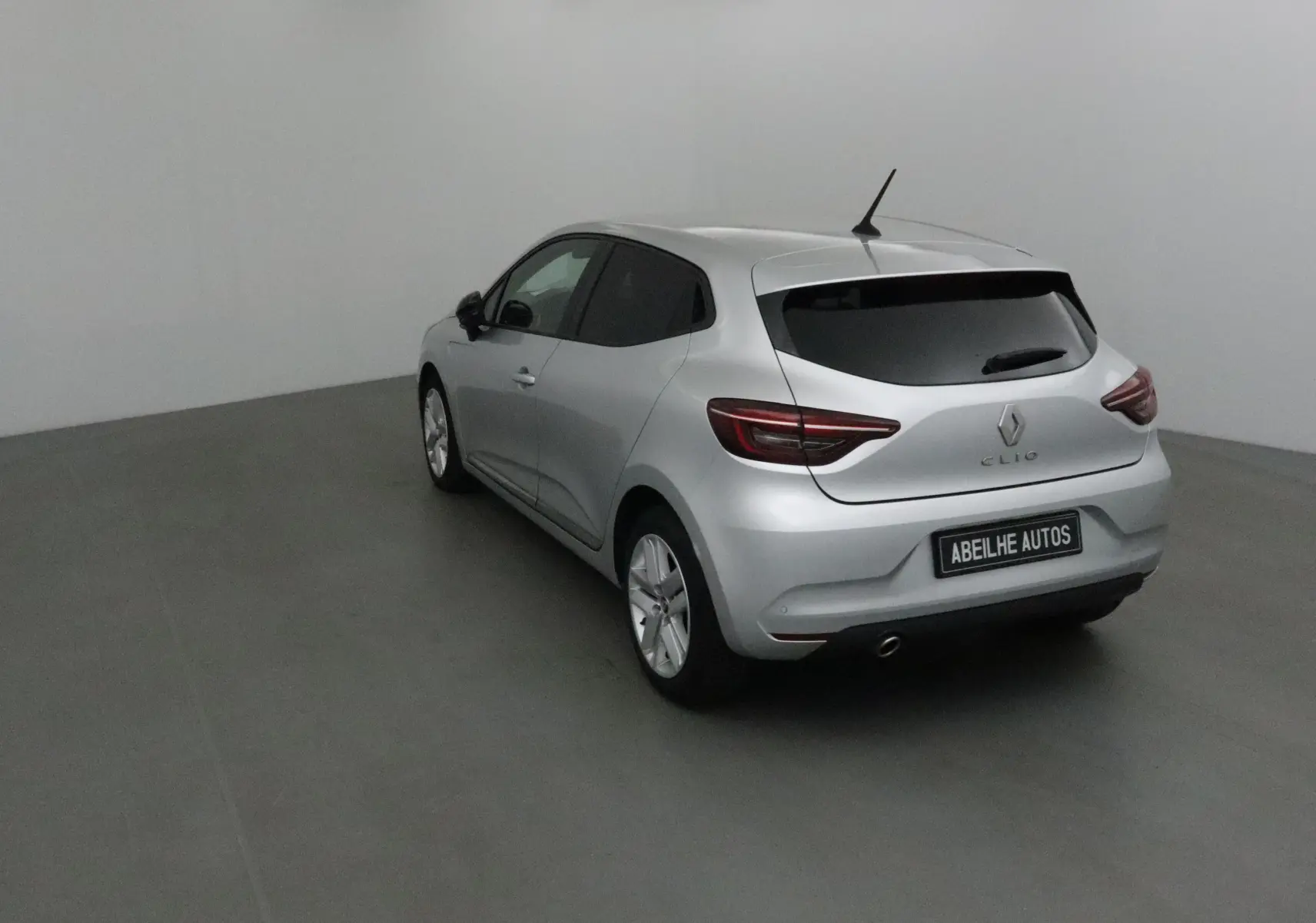 Renault Clio V gris platine vue 3/4 arrière côté gauche dans un studio avec vitres teintées et antenne toit.