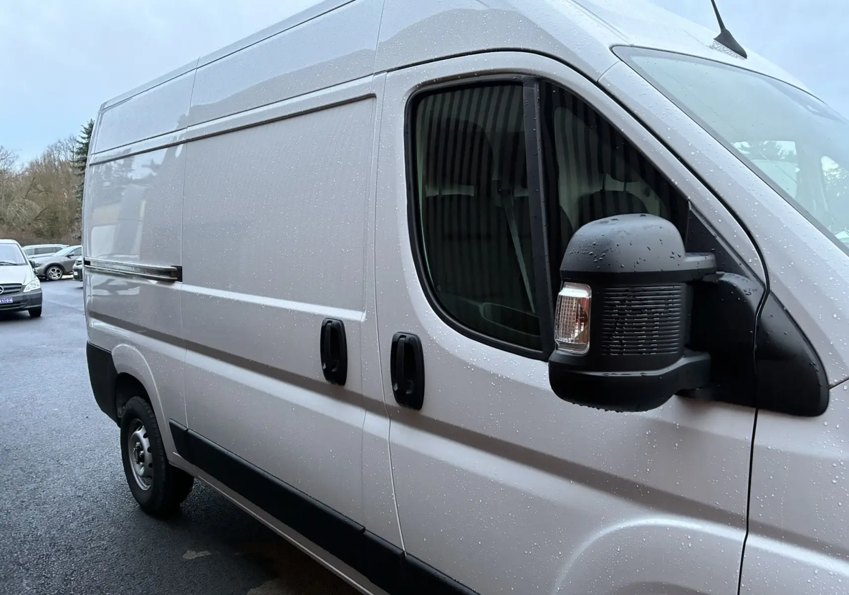 Vue de profil droit d’un FIAT Ducato Fourgon blanc 2025 avec portes coulissantes et rétroviseur noir sous la pluie.