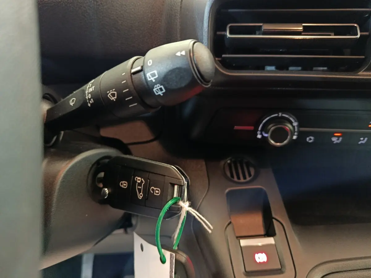 Gros plan intérieur sur la clé insérée dans le contacteur d’un Peugeot Partner blanc, avec commandes de climatisation visibles.