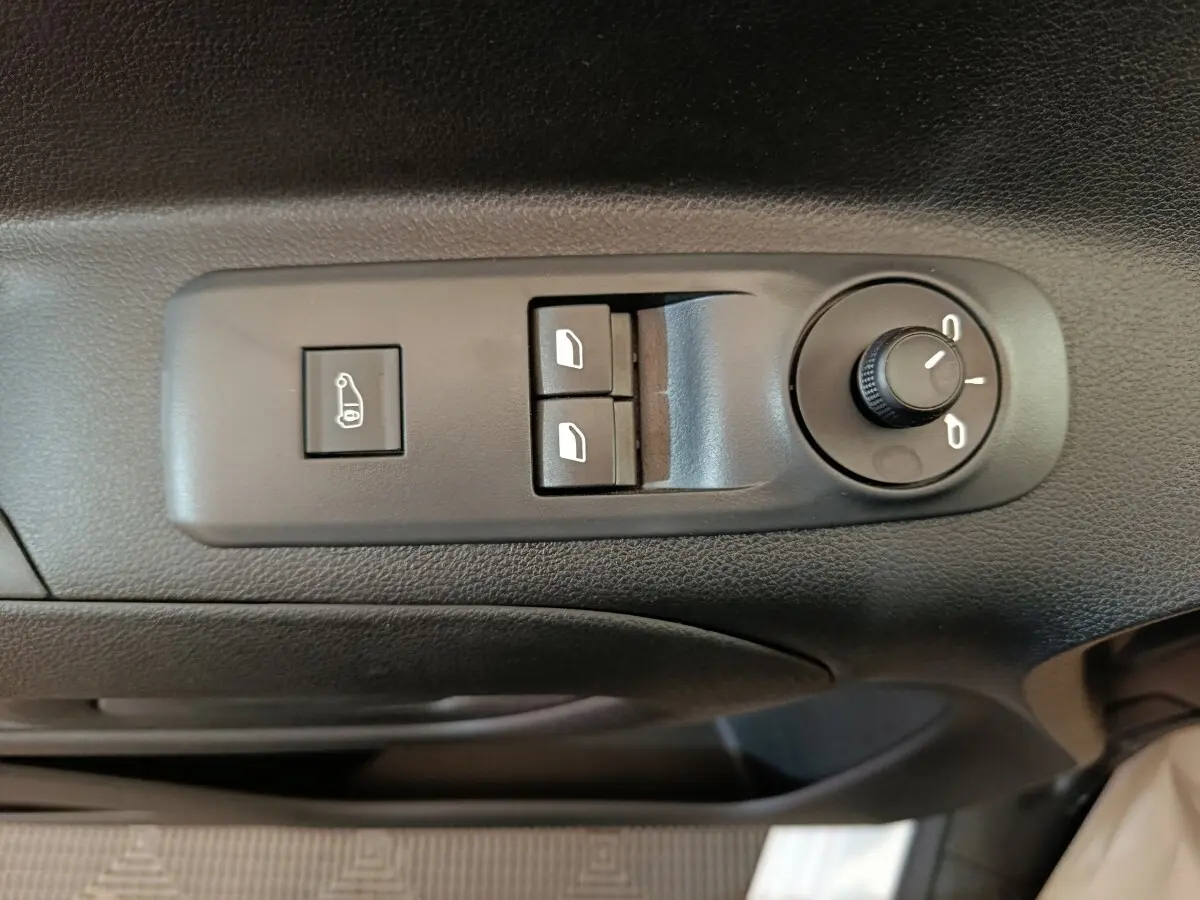 Vue rapprochée des commandes de réglage des rétroviseurs et des vitres électriques sur la porte côté conducteur d’un Peugeot Partner blanc.