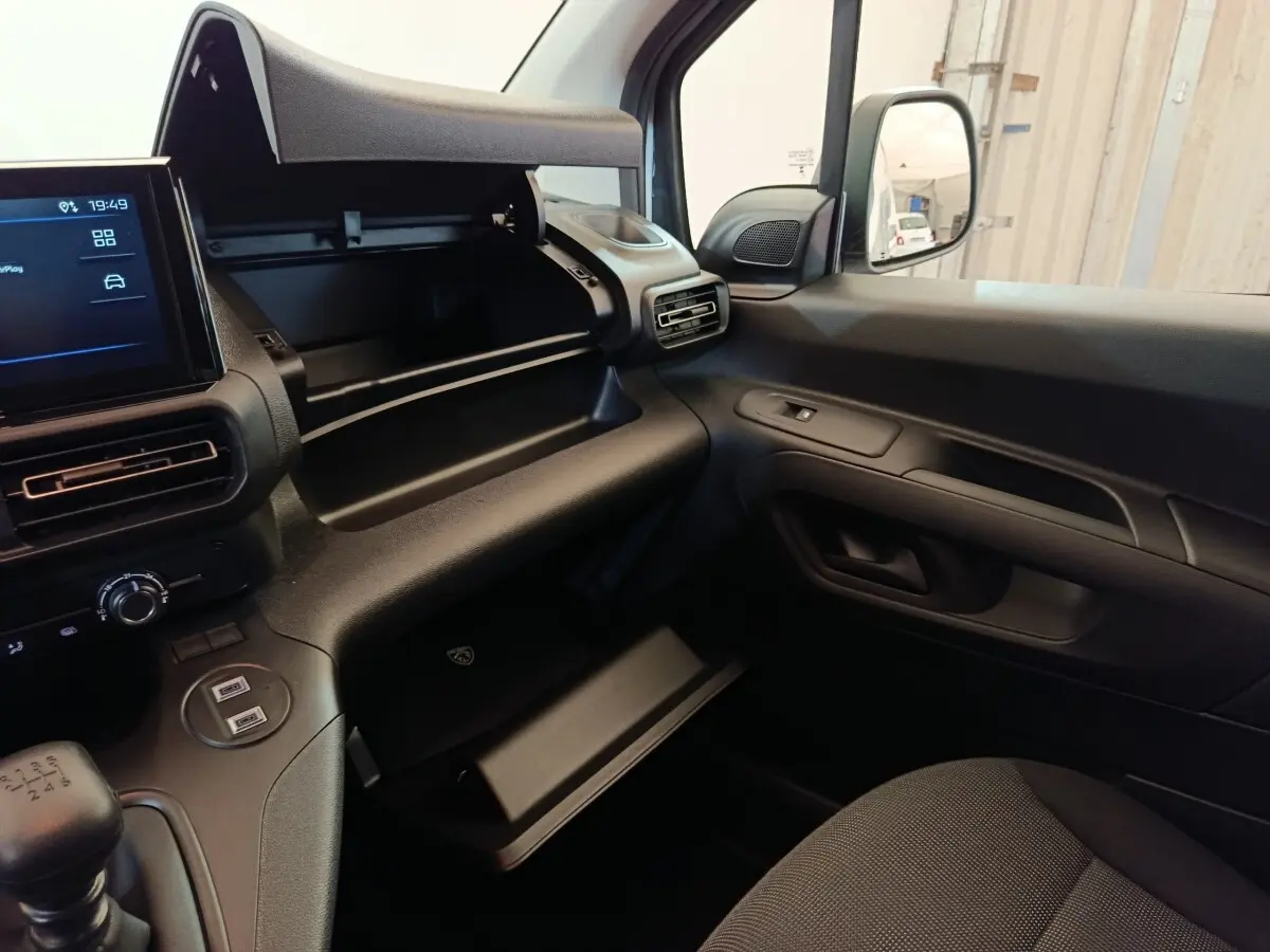 Vue intérieure côté passager du Peugeot Partner 2025 blanc, montrant tableau de bord et boîte à gants ouverte.