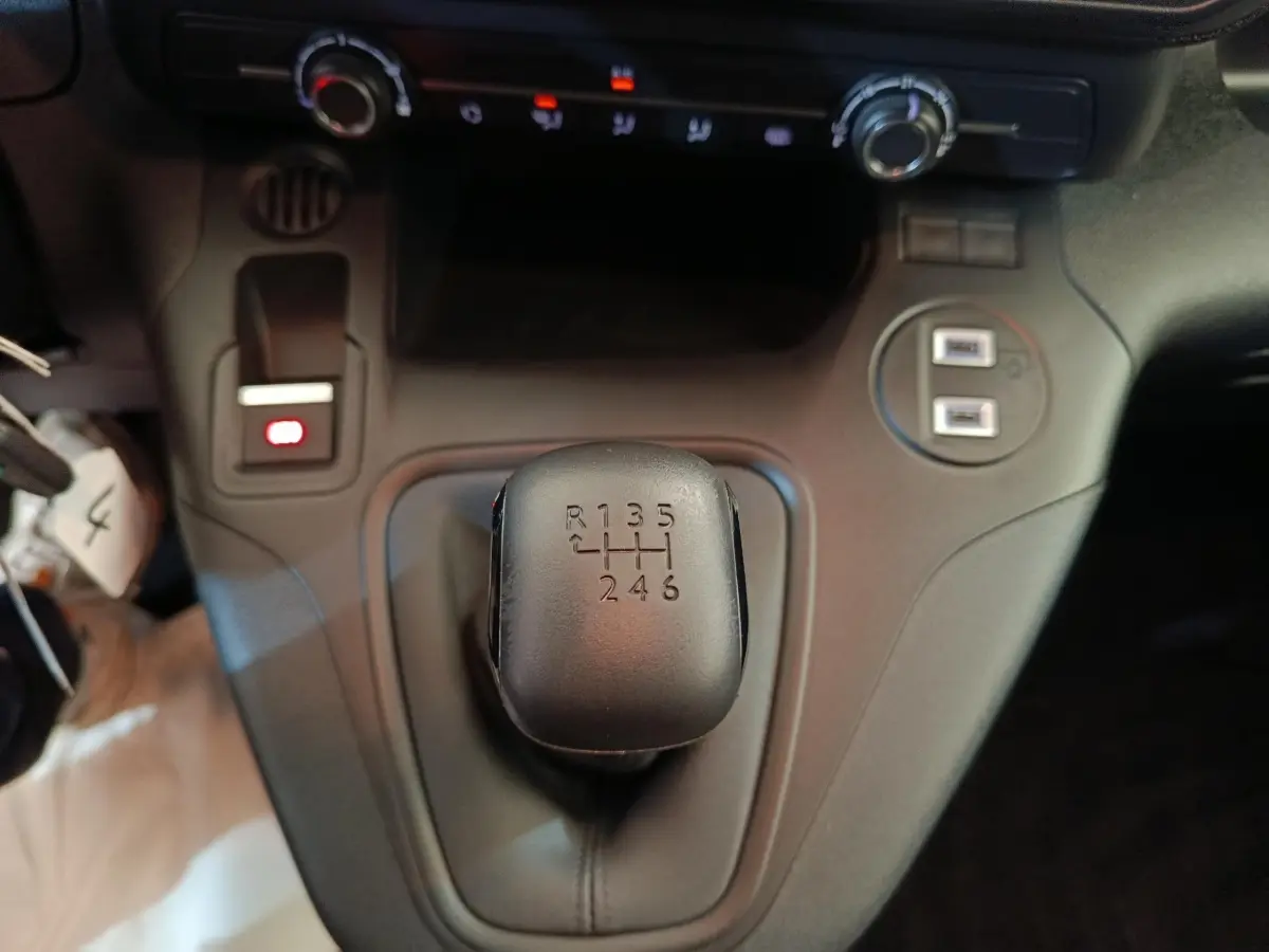 Gros plan sur le levier de vitesses manuel noir du Peugeot Partner blanc, avec commandes de climatisation en arrière-plan.