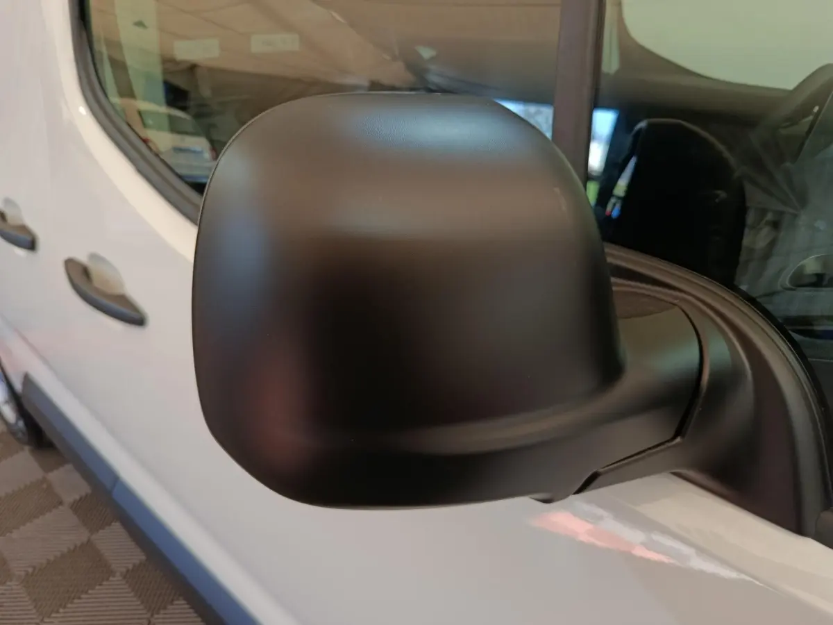 Rétroviseur noir en gros plan sur le côté gauche d’un Peugeot Partner blanc, vue partielle du véhicule.