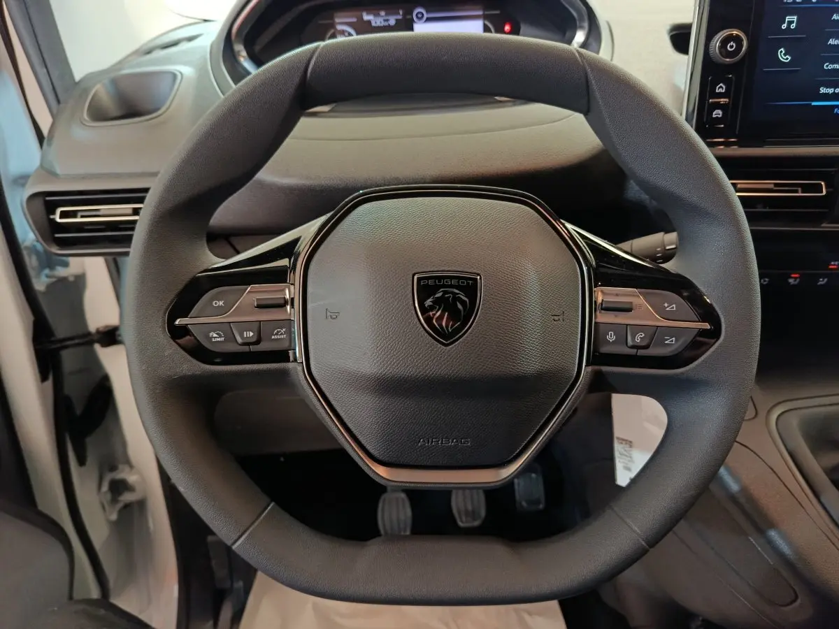 Vue rapprochée du volant multifonction noir du Peugeot Partner blanc 2025, avec logo lion central et commandes intégrées.