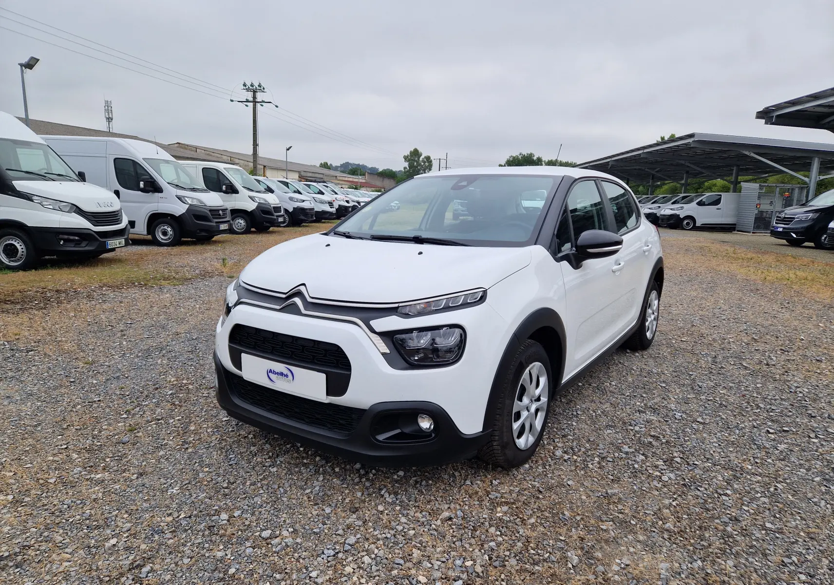Citroën C3 Société blanc vue 3/4 avant droit sur parking avec plusieurs utilitaires en arrière-plan.
