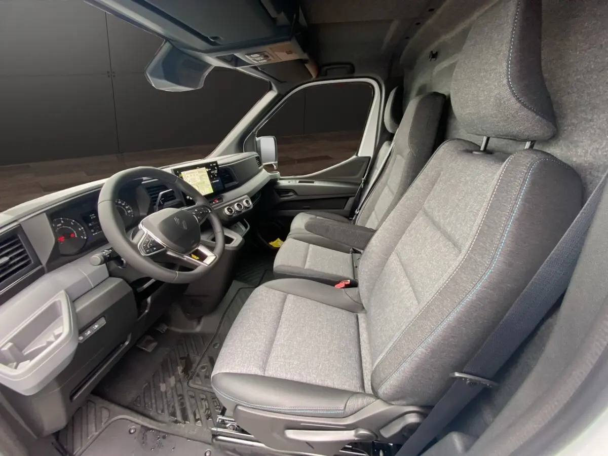 Vue intérieure côté conducteur du Renault Master 2026, sièges gris avec surpiqûres bleues et tableau de bord moderne.