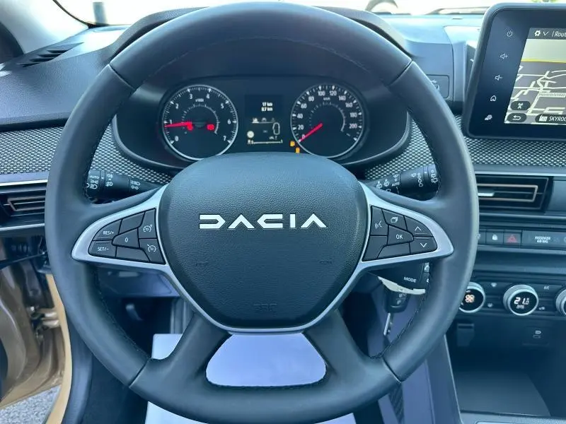 Vue rapprochée du volant noir de la Dacia Sandero beige Safari 2025 avec commandes intégrées et tableau de bord visible.