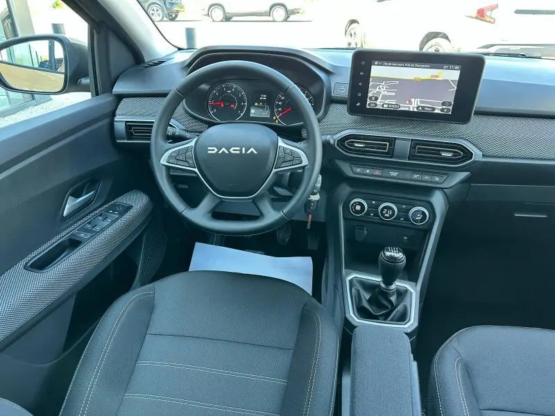 Vue intérieure avant de la Dacia Sandero 2025, tableau de bord avec écran tactile et volant multifonction noir.