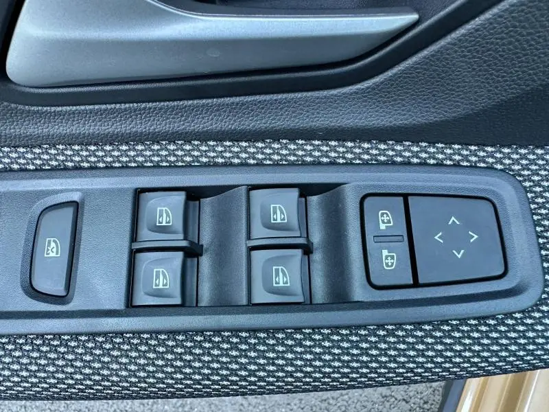 Commandes électriques des vitres et réglages des rétroviseurs sur la porte côté gauche d'une Dacia Sandero beige Safari 2025.