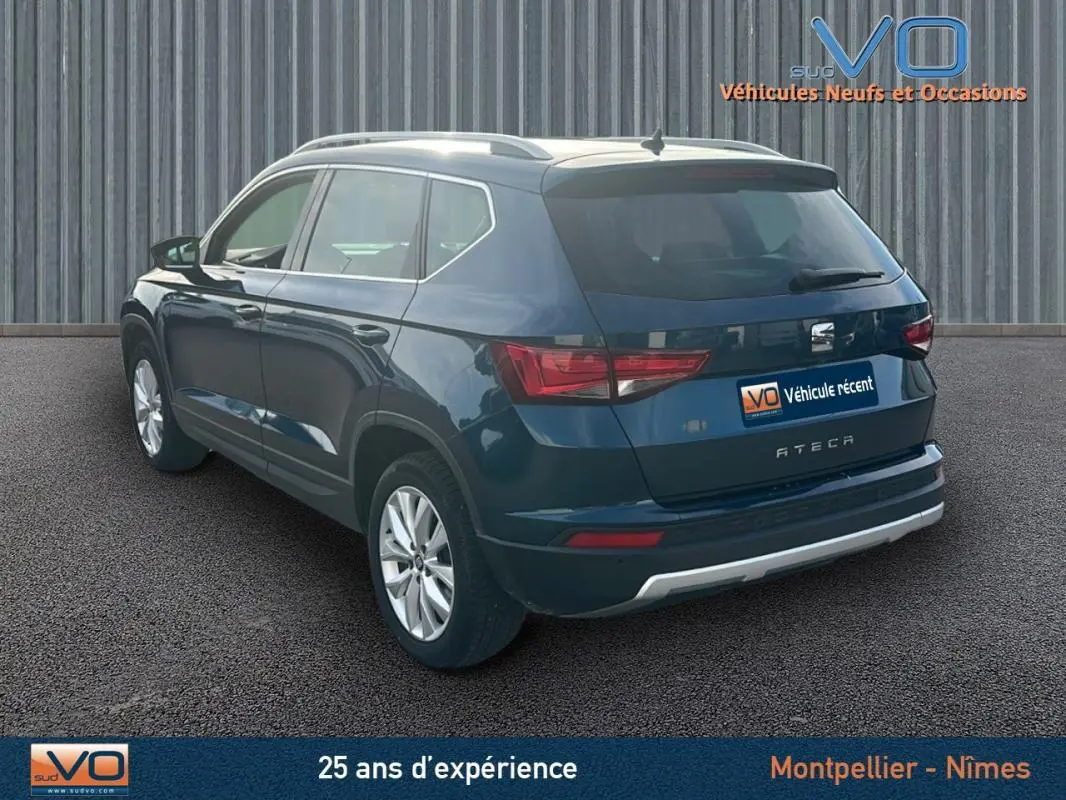 Vue 3/4 arrière droite d'un SEAT Ateca bleu foncé avec jantes alliage et barres de toit visibles.
