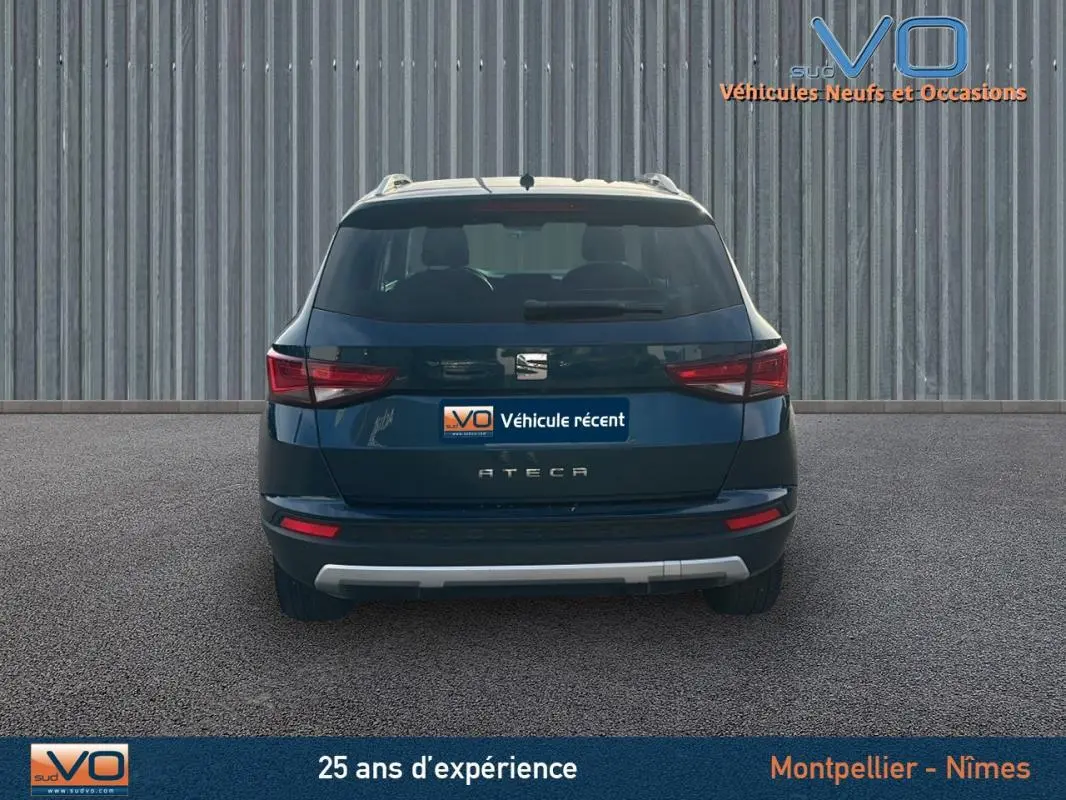 Vue arrière d'un SEAT Ateca bleu foncé avec feux arrière allumés et logo central visible sur fond industriel.