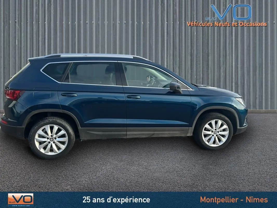 Profil latéral droit d'un SUV SEAT Ateca bleu foncé avec jantes alliage 17 pouces, stationné devant un mur métallique.