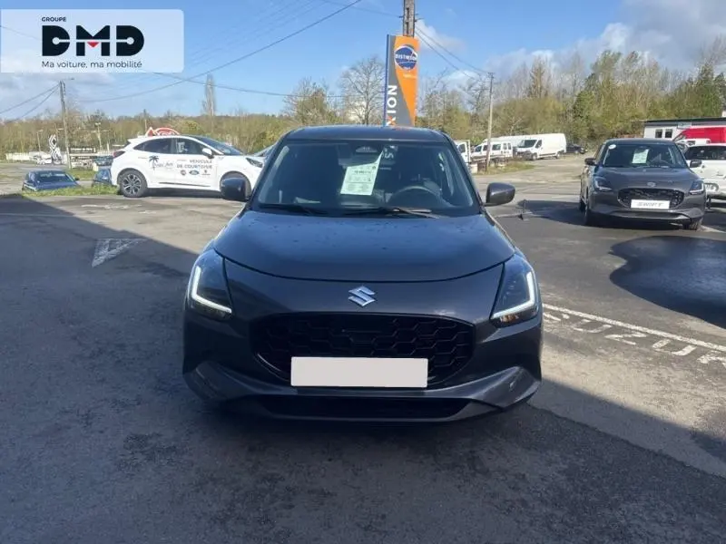 Vue avant d'une Suzuki Swift 1.2 Hybrid 83ch Privilège gris minéral avec calandre noire et phares LED allumés.