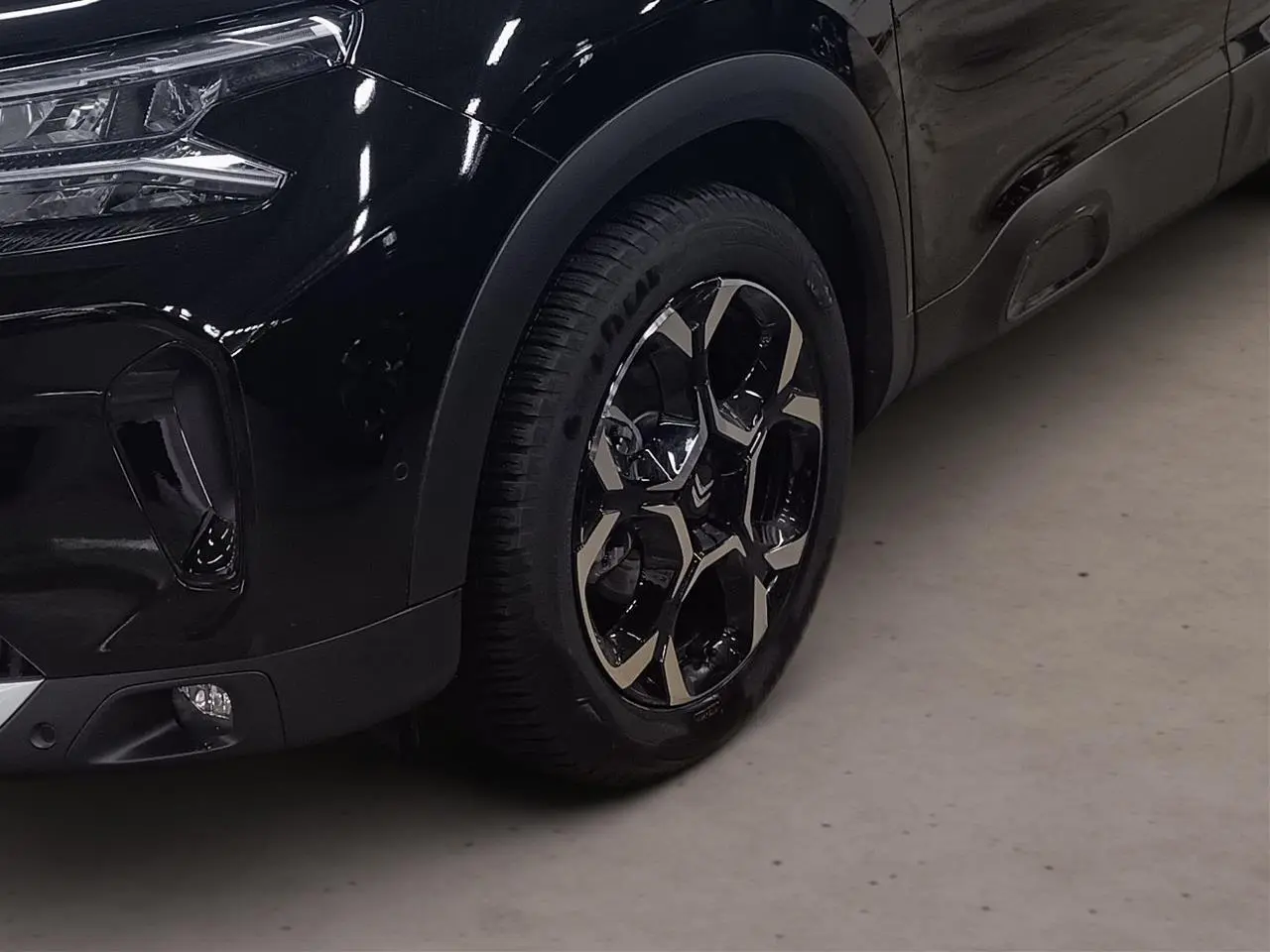 Gros plan sur la roue avant droite et le pare-chocs avant noir Perla du Citroën C5 Aircross Hybrid 2025.