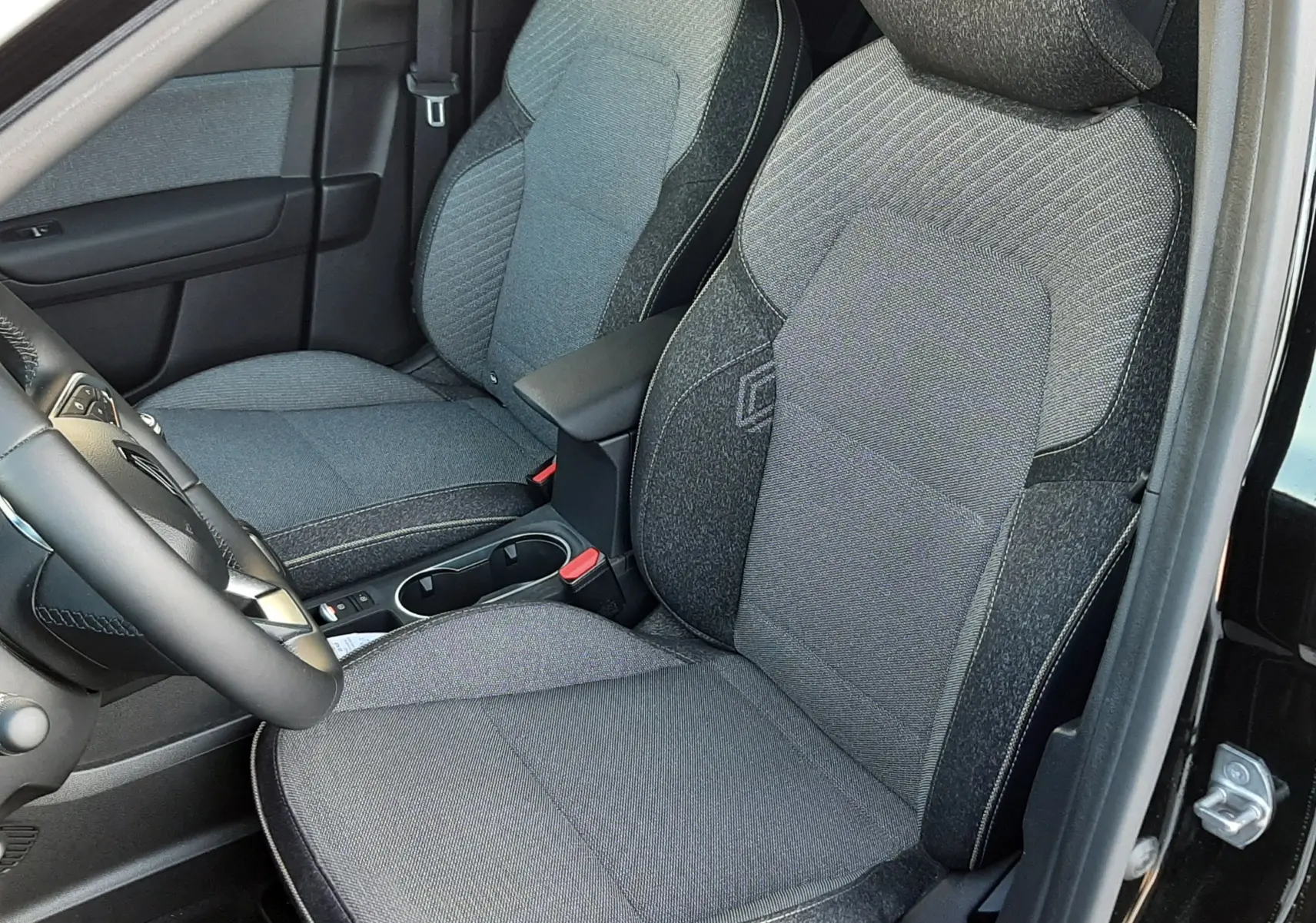 Vue intérieure côté conducteur du Renault Captur 2024 noir métal, sièges tissu gris avec logo Renault brodé.