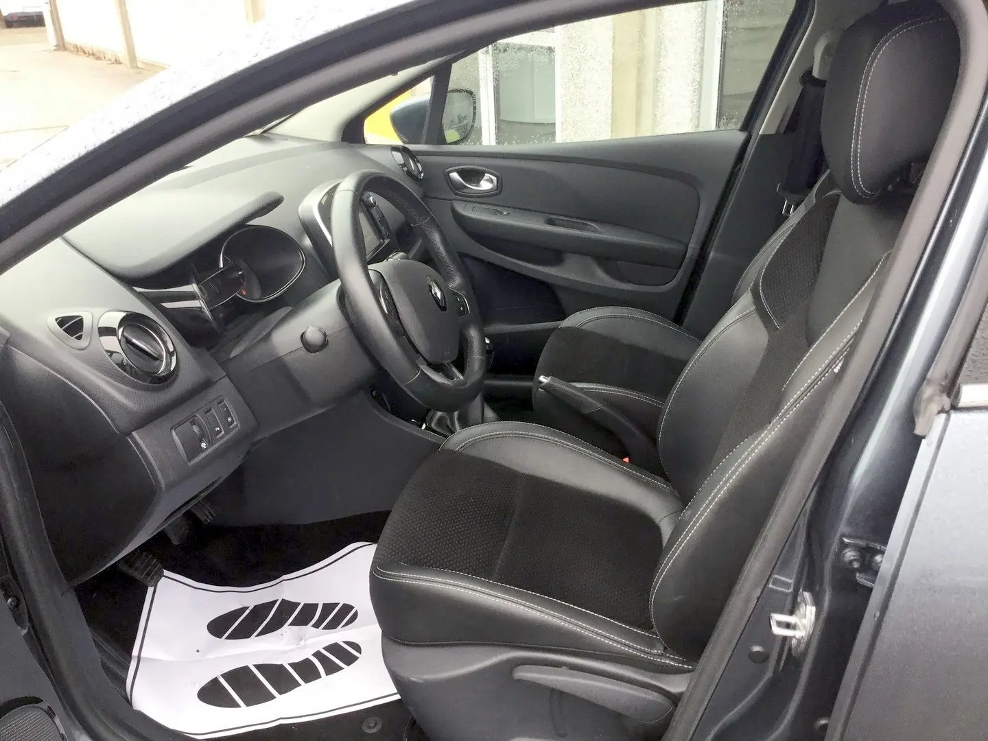 Vue intérieure côté conducteur de la Renault Clio IV Estate gris titanium, montrant les sièges en cuir et le tableau de bord.