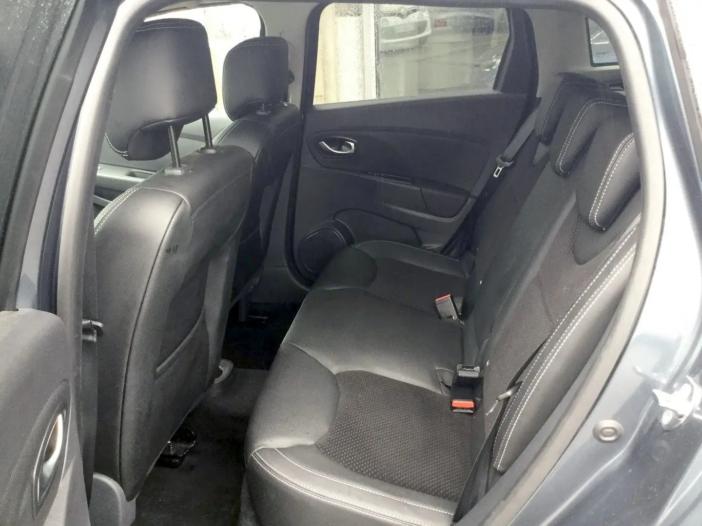 Vue intérieure côté arrière droit de la Renault Clio IV Estate gris titanium, sièges arrière en cuir noir avec surpiqûres blanches.
