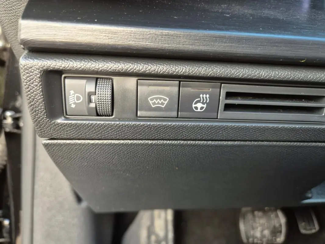 Gros plan sur les commandes noires côté gauche du tableau de bord de la Citroën C5 X 2024, avec bouton de réglage des phares et chauffage du volant.