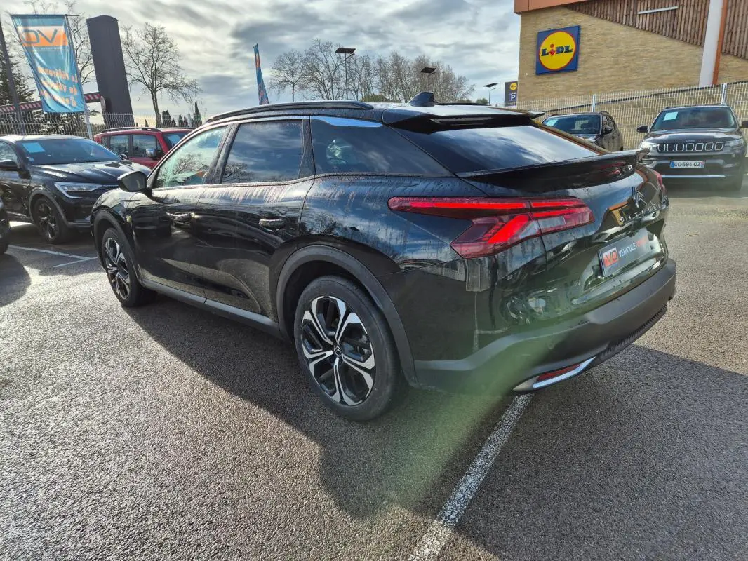 Vue 3/4 arrière droite d'une Citroën C5 X noire 2024 avec jantes alliage 19 pouces et antenne requin sur parking.